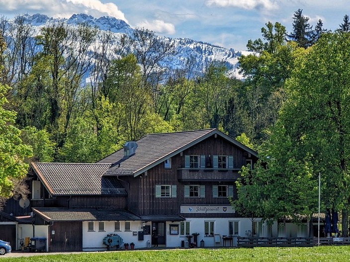 Der Schützenwirt im Priener Eichental, dahinter Bäume und die verschneiten Chiemgauer Berge